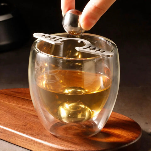 Placing a Coffee Ice Sphere Maker Stainless Steel Ball Mold in a glass for cold brew iced coffee on wooden tray.