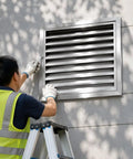 A person installing a Tough As Nails Stainless Steel Louvered Grille Access Panel For Drywall Ventilation and Outdoor Plumbing Inspection Door.