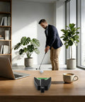 Man using Automatic Golf Putting Machine For Indoor And Outdoor Practice Portable Ball Return System with plants and laptop nearby.