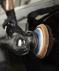 Side view of black nitrile disposable gloves on hands while a technician polishes a car with a buffer.