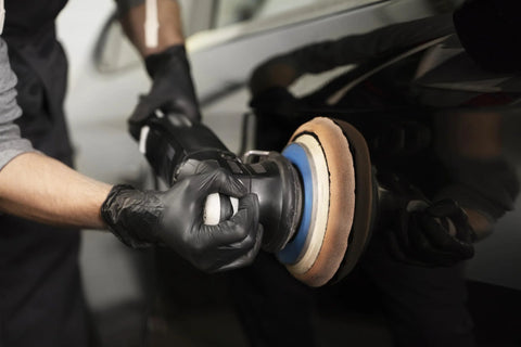 Side view of black nitrile disposable gloves on hands while a technician polishes a car with a buffer.