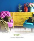 Colorful interior featuring a pink and blue velvet chair with cushions, and a yellow cabinet adorned with vases and flowers.