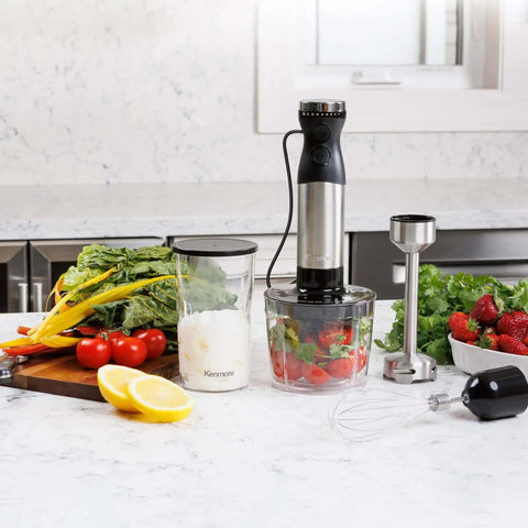 Badass Handheld Immersion Blender With Turbo Pulse Power And Four Rock Solid Stainless Blades, Includes Quick Snap Chopper Bowl And Wire Whisk To Crush Blending Jobs Without Breaking A Sweat on a kitchen counter with vegetables.