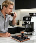 Man enjoying coffee beside Heavy Duty Wooden Espresso Tamper Station Holder Fits 51mm To 58mm Portafilters in kitchen.