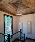 4-Light Farmhouse Drum Chandelier in stairway, barn-inspired with rustic wood rings, black metal finish, natural wood accents.