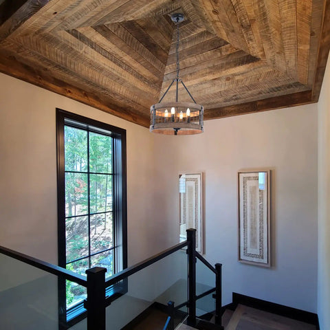 4-Light Farmhouse Drum Chandelier in stairway, barn-inspired with rustic wood rings, black metal finish, natural wood accents.