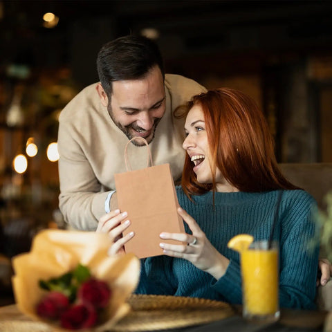 Couple exchanging Small Brown Kraft Gift Bags With Handles Five And A Quarter By Three And Three Quarter By Eight Inches 50 Pcs Heavy Duty 100 GSM Kraft Paper Great For Small Biz Gift Wrapping Party Favors Birthday Bags Shopping Made In USA in a cozy restaurant setting