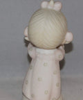 Back view of a porcelain figurine of a child in a pink dress with flower details, showcasing fine craftsmanship.