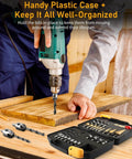 Front view of a green power drill drilling wood; 34-piece woodworking drill bit set in a black plastic case nearby.