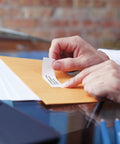 Person applying Top Shelf Peel And Stick Mailing Address Labels For Thermal Printers White Adhesive Tape 1 1/8 X 3 1/2 Inches on an envelope.