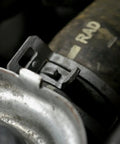 Close-up of a metal hose clamp on a radiator hose with Super Handy Flexible Cable Hose Clamp Pliers That Lock To Free Your Hands While Removing Plastic Or Metal Self Tightening Clamps In Sizes From Eleven Sixteenths Inch Up To Two And A Half Inches For Those Hard To Reach Auto Repair Jobs in use, showing clamp details.