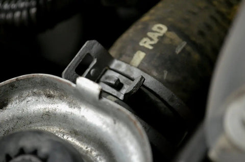 Close-up of a metal hose clamp on a radiator hose with Super Handy Flexible Cable Hose Clamp Pliers That Lock To Free Your Hands While Removing Plastic Or Metal Self Tightening Clamps In Sizes From Eleven Sixteenths Inch Up To Two And A Half Inches For Those Hard To Reach Auto Repair Jobs in use, showing clamp details.