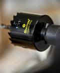 Close-up of Carbide Tipped Hole Saw With Premium Finish For Wood PVC And Fiberglass Four And Three Quarters Inch Diameter One And Five Eighths Inch Cutting Depth Three Teeth Per Inch Built Tough For Real Pro Jobs CT434 attached to a drill.