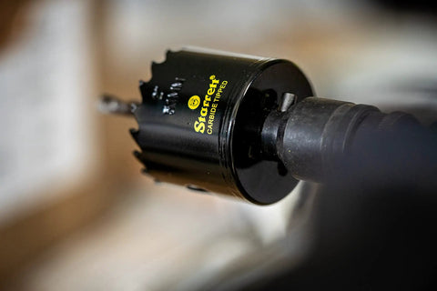 Close-up of Carbide Tipped Hole Saw With Premium Finish For Wood PVC And Fiberglass Four And Three Quarters Inch Diameter One And Five Eighths Inch Cutting Depth Three Teeth Per Inch Built Tough For Real Pro Jobs CT434 attached to a drill.