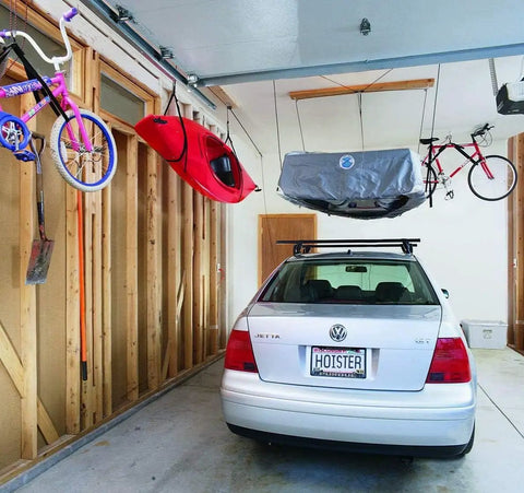 Overhead Garage Hoist System For Lightweight Cargo Carrier To Tuck Kayaks Canoes And Paddle Boards Up High Four Point Hoist 60 LB Max Per Carrier Fits 16 Ft Ceilings Easy One Person Install in use with kayak and cargo overhead in a garage.