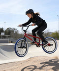 Kid jumping on Freestyle 20 Inch BMX Bike For Beginners Kids 8 To 15 Red Frame with Blue Tires in skate park