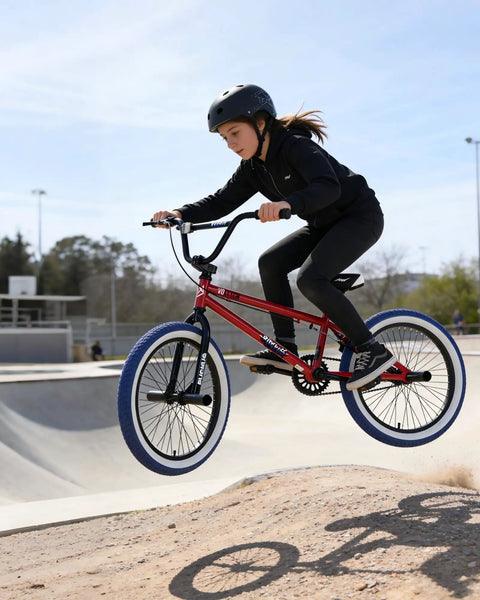 Kid jumping on Freestyle 20 Inch BMX Bike For Beginners Kids 8 To 15 Red Frame with Blue Tires in skate park