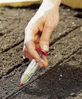Compact Handheld Seed Spreader For Precise Sowing In Lawns, Gardens And Planters in use on soil bed.