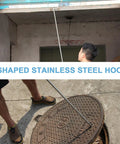Heavy Duty Stainless Steel Manhole Cover Hook With Sturdy T Shaped Handle Design lifting a manhole cover with human feet visible.