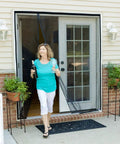 Woman walking through Magnetic Screen Door For French And Sliding Doors, Heavy-Duty Hands-Free Fiberglass Mesh With Self-Closing Magnetic Seal, Black Trim, Fits 70x80 Inch Doors, Screen Size 72x82 installed in a home.