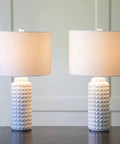 Felix LED Ceramic Table Lamps Set Of 2 In Antique Brass Finish With White Linen Hardback Shade, shown on dark surface