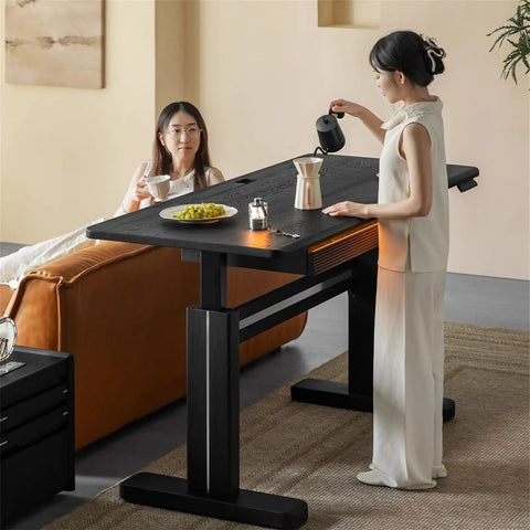 Super Sturdy Electric Standing Desk With Dual Storage Drawers And Whisper Quiet Lift Features A Heavy Duty Ash Wood Desktop In Crisp Matte Black, woman pouring coffee.