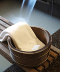 Wooden spa bucket with towel beside flowing water, portable sauna steamer joint hose connector is not visible