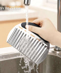 Stainless steel potato crinkle cutter with black handle; hand-held side view under running water.
