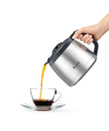 Hand pouring coffee from brushed stainless steel carafe into glass cup, part of Grind Control Coffee Maker With Built In Grinder.