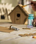Close-up of Cricut knife blade and drive housing on a wooden craft table with cardboard pieces.