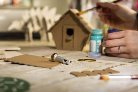 Close-up of Cricut knife blade and drive housing on a wooden craft table with cardboard pieces.