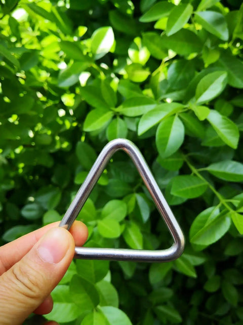 Hand holding a Stainless Steel 316 Marine Grade Triangle Ring Buckle Welded V Shaped for tie-down against green leaves.