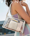 Woman holding clear shoulder bag with visible phone, Vlando pouch, and magazine in outdoor setting.