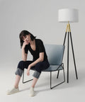 Levi LED Floor Lamp With Tall Black And Gold Tripod For A Dope Living Room Vibe next to seated person, modern decor style.
