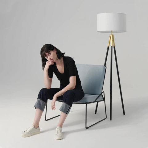Levi LED Floor Lamp With Tall Black And Gold Tripod For A Dope Living Room Vibe next to seated person, modern decor style.