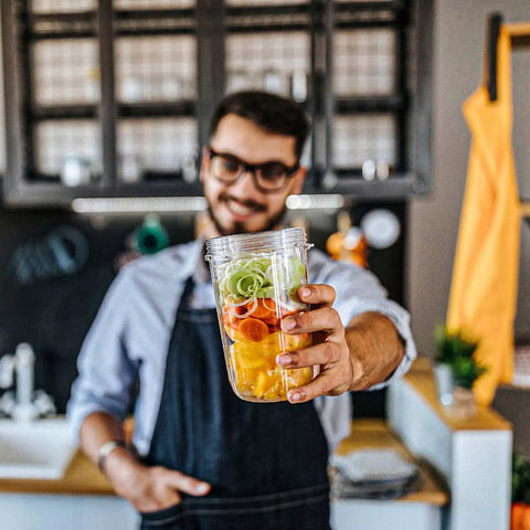 Man in apron holding 2 Pack 32oz Replacement Cups For 600W And 900W Blenders with fresh ingredients inside.