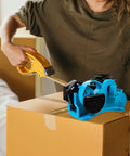 Semi Automatic Heat Tape Cutter With Compact Desktop Packing Station And Lightweight Tape Holder For Quick Box Sealing And Top Shelf Shipping Hustle The Reliable Gadget For Smooth Tape Dispensing Routine Blue in use on a cardboard box.