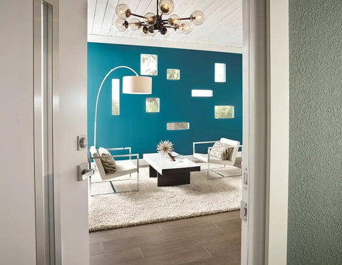 View from a partially opened door with Northbrook Satin Nickel Door Lever With Keyed Entry, Exterior Key Access And Interior Turn Button For Easy Locking, Durable Finish That Coordinates With Lighting And Plumbing Fixtures And Other Home Hardware into a modern living room with blue walls, white furniture, and modern lighting.