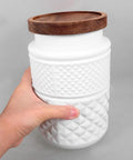 Vintage Matte White Glass Storage Jars With Airtight Wood Lids 1800ML Set Of 2 held in hand with textured design.