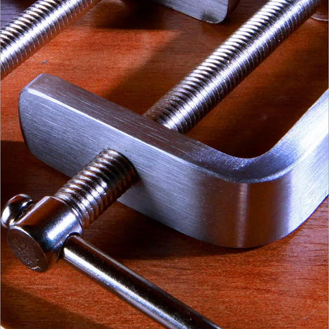 Stainless steel C-clamp with threaded screw, close-up on wooden workbench.