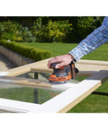 Badass 18V Cordless Orbital Sander With Killer Dust Control And Super Smooth Softgrip Handle For Hassle Free Wood Projects 12,000 Opms Compact Orange Design in use on a wooden door.