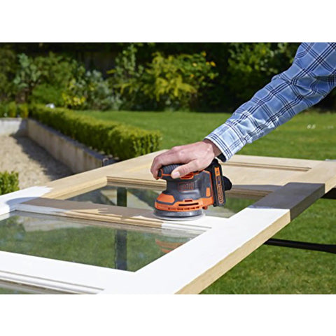 Badass 18V Cordless Orbital Sander With Killer Dust Control And Super Smooth Softgrip Handle For Hassle Free Wood Projects 12,000 Opms Compact Orange Design in use on a wooden door.