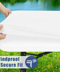 Hands stretching a white tablecloth over a table, showcasing the windproof and secure fit feature with scenic outdoor background.