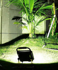 JUDYSSY Spot Lighting Led Floodlight 100W Led Outdoor Flood Lights illuminating grass and palm in an outdoor setting at night.