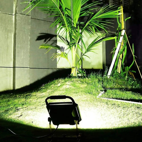 JUDYSSY Spot Lighting Led Floodlight 100W Led Outdoor Flood Lights illuminating grass and palm in an outdoor setting at night.