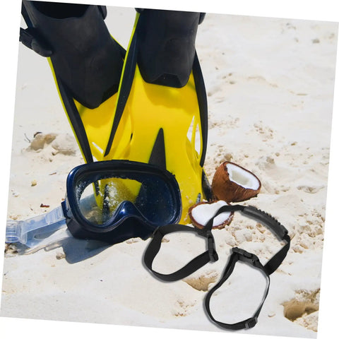 Yellow diving fins, snorkeling mask, and stretchy diving tank cylinder band retainer for scuba gear on sandy beach.