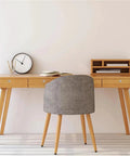 Modern wooden desk with drawers, a clock, books, and a gray chair in a minimalistic setting.