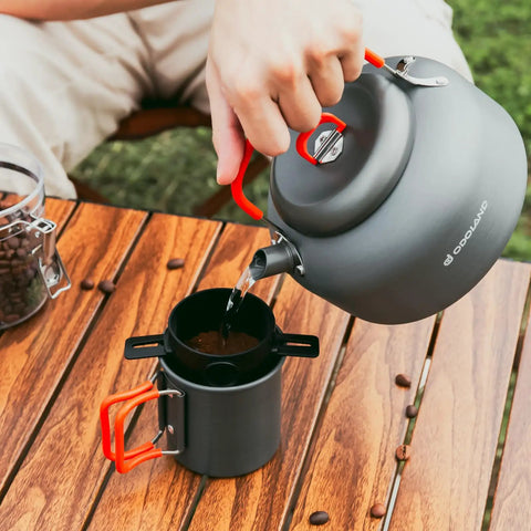 Pouring water from a kettle into a percolator on a wood table, part of the 1.2L Camping Coffee Pot Set With Kettle, Mug And Percolator For Stove Top Brewing, Durable Aluminum Outdoor Coffee Kit For Two, Great For Hiking, Campfires And Weekend Getaways.