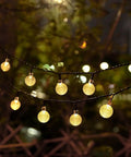 Battery Operated Globe Fairy Lights 16 Feet Waterproof With Timer And 8 Modes 30 LEDs Warm White Indoor Outdoor Decor For Patio Garden Christmas Tree 2 Pack Create Cozy Vibes glowing at night in garden setting.