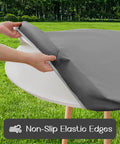 Round Vinyl Tablecloth With Elastic Edge And Flannel Backing, No-Slip No-Fuss 100 Percent Waterproof Fitted Cover For 36 To 44 Inch Tables, Wipeable Plastic Table Cloth For Picnic And Outdoor Use, Grey being installed on a round table outdoors.